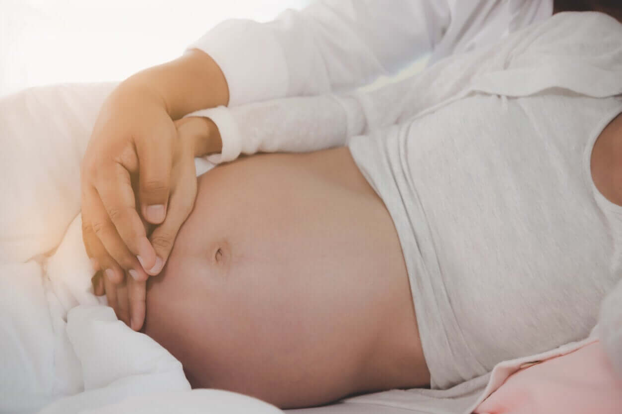 A pregnant woman and her partner lying in bed with their hands on her belly.