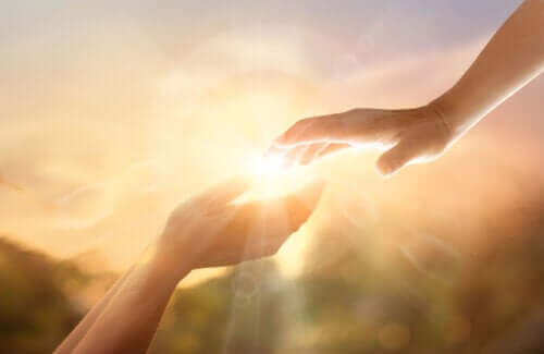 Two hands touching with the sun shining in the background.