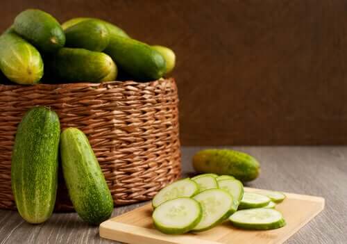 Sliced cucumbers on a cutting board next to a basket of whole cucumbers.