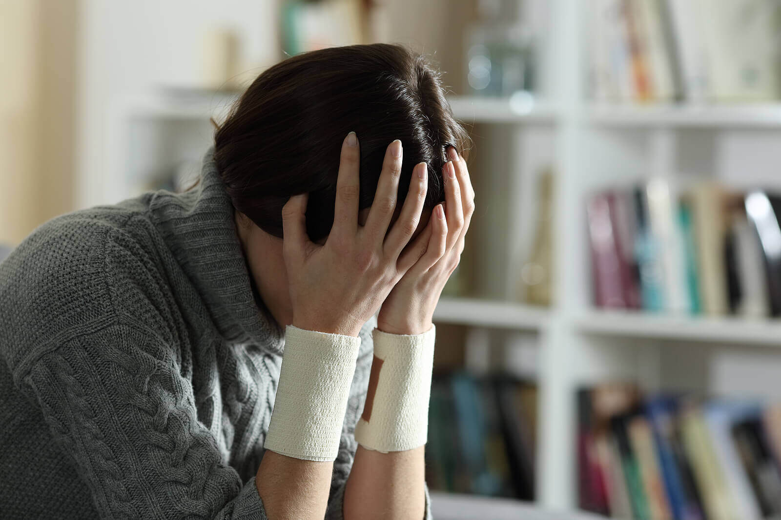 En kvinna med bandage på armarna som håller sitt huvud.