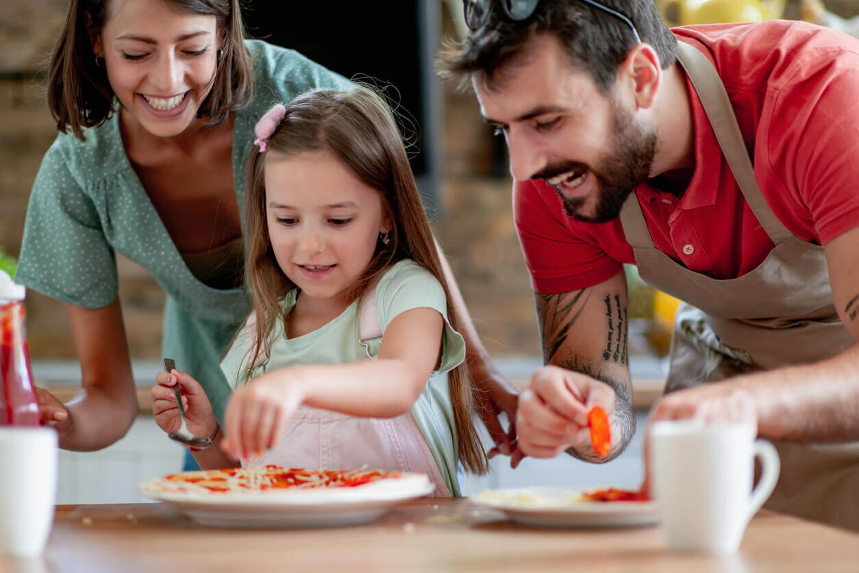 Parents helping their daughter make pizza.