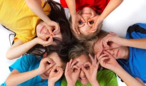 Children lying on the floor with their heads together, looking up, with their hands over their eyes like binoculars.