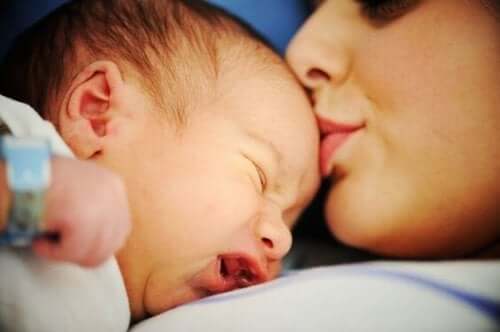 A mother kissing her fussy newborn on the forehead.