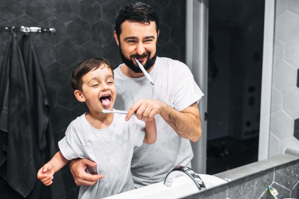 A dad helping his son brush his teeth.