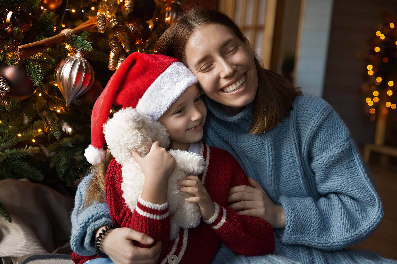 A mother and daughter hugging by the Christmas tree.
