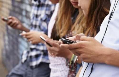 Teens leaning against the wall looking at their cell phones.