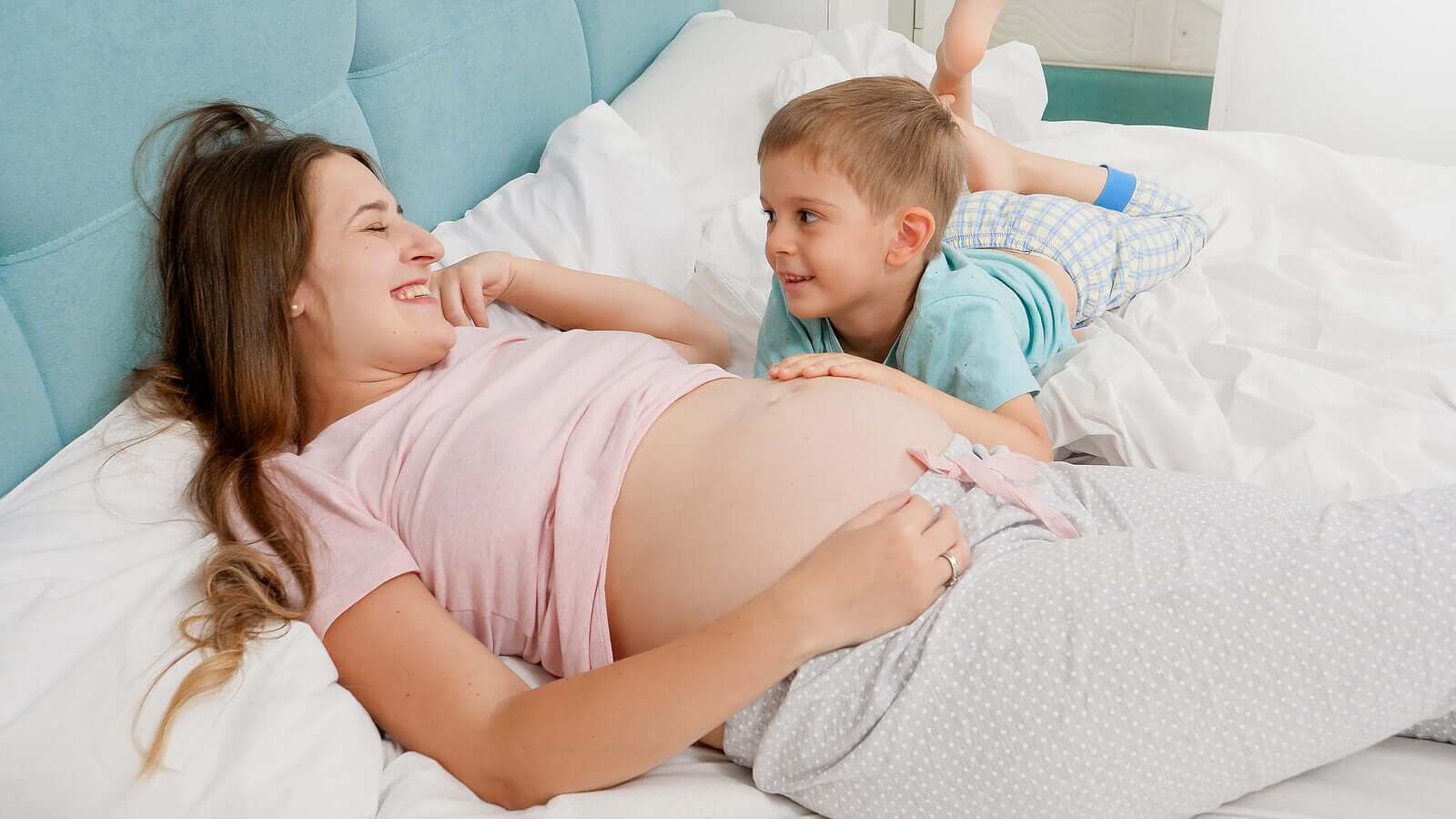 A pregnant woman lying in bed while her son puts his hand on her growing belly.