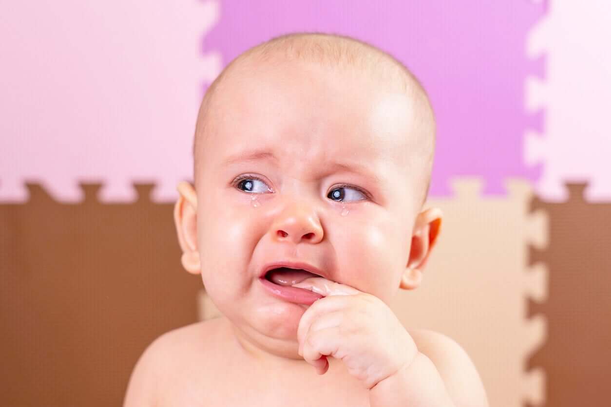 A teething baby with his finger in his mouth, crying.