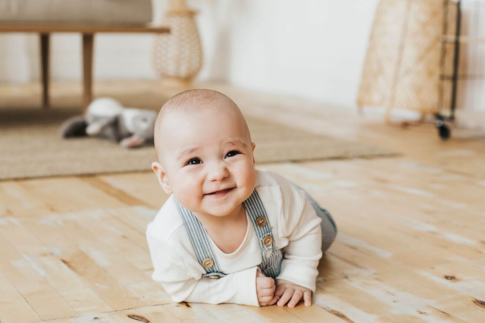 A baby lying face down on the floor and smiling.