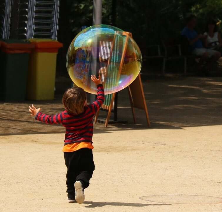 A baby running after a giant soap bubble.