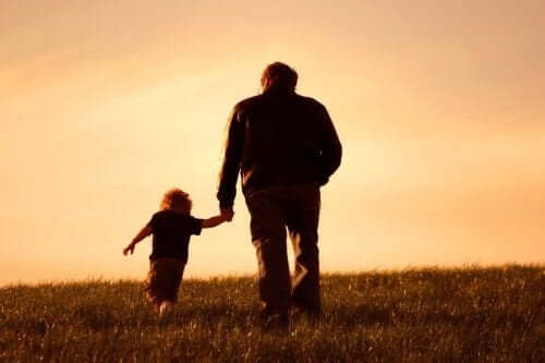 A grandfather and grandson walking in a field at sunset, holding hands.
