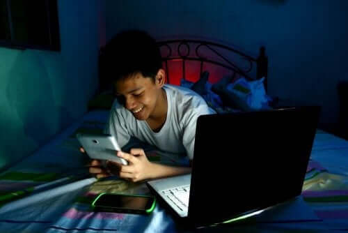 A child lying in bed in the dark playing video games.