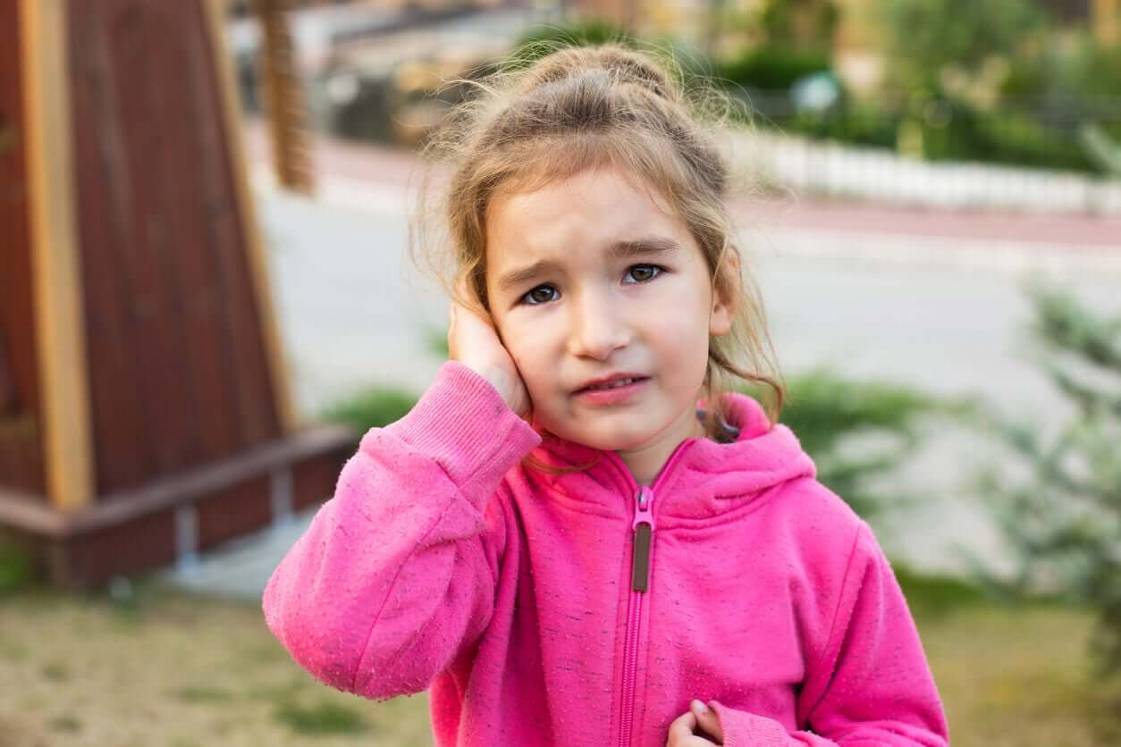 Et barn som holder hånden over høreøret og ser ut som hun har det vondt.