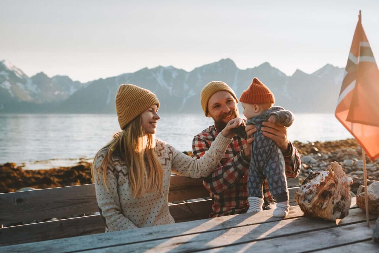 Two parents in Norway playing with their son on the shore, with mountains in the distance.