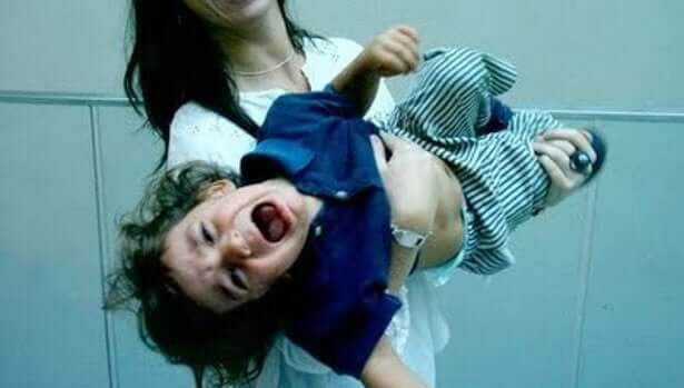 A mother carrying a toddler who's having a temper tantrum.