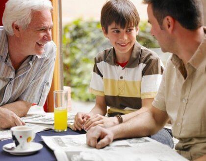 A preteen boy sitting at the table with his father and grandfather.