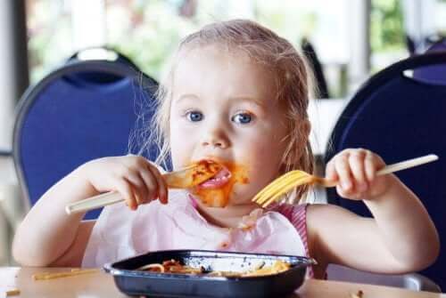 En liten flicka som matar sig själv med spagetti på en restaurang.