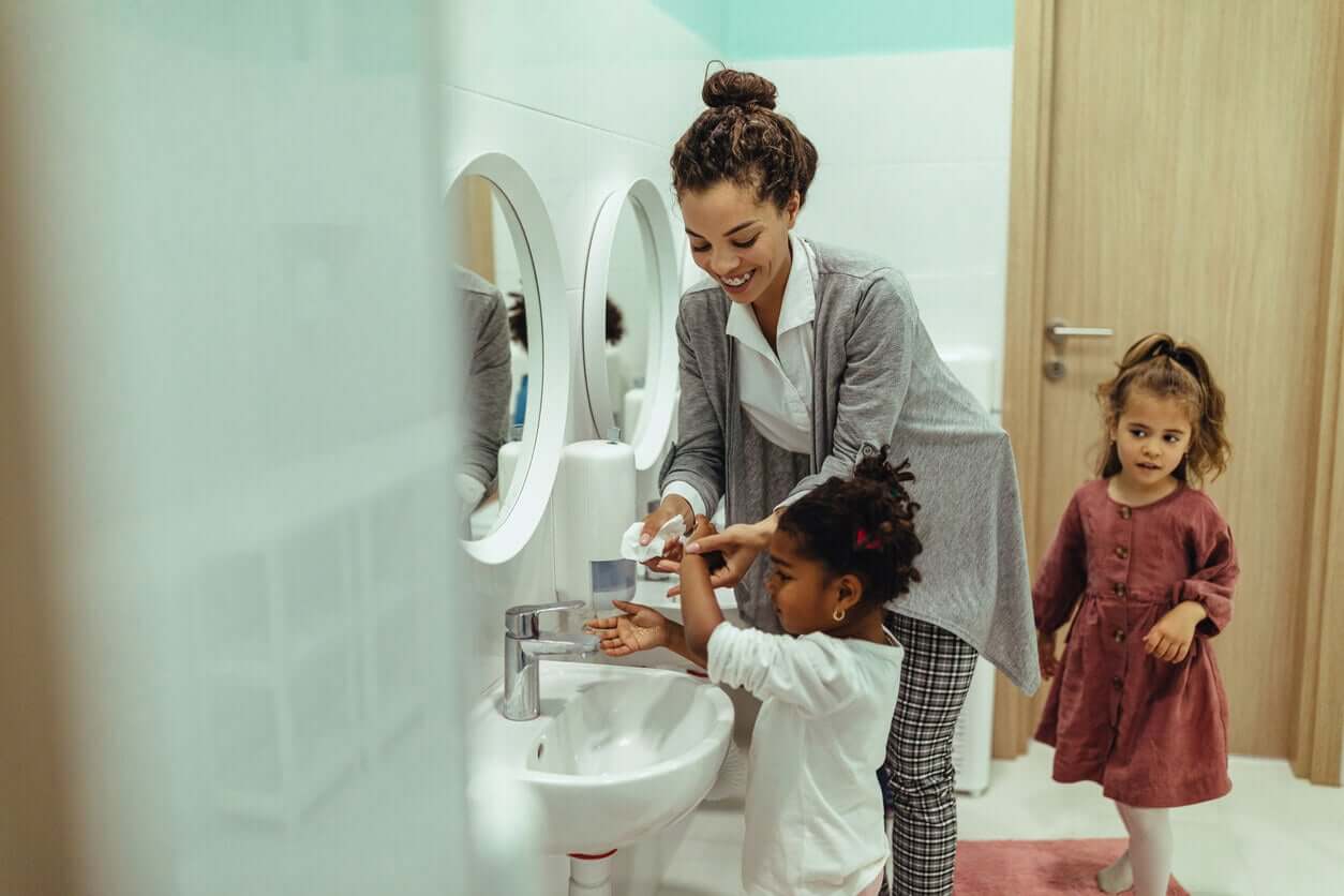 A mother washing her daughter hands in the bathroom sink.