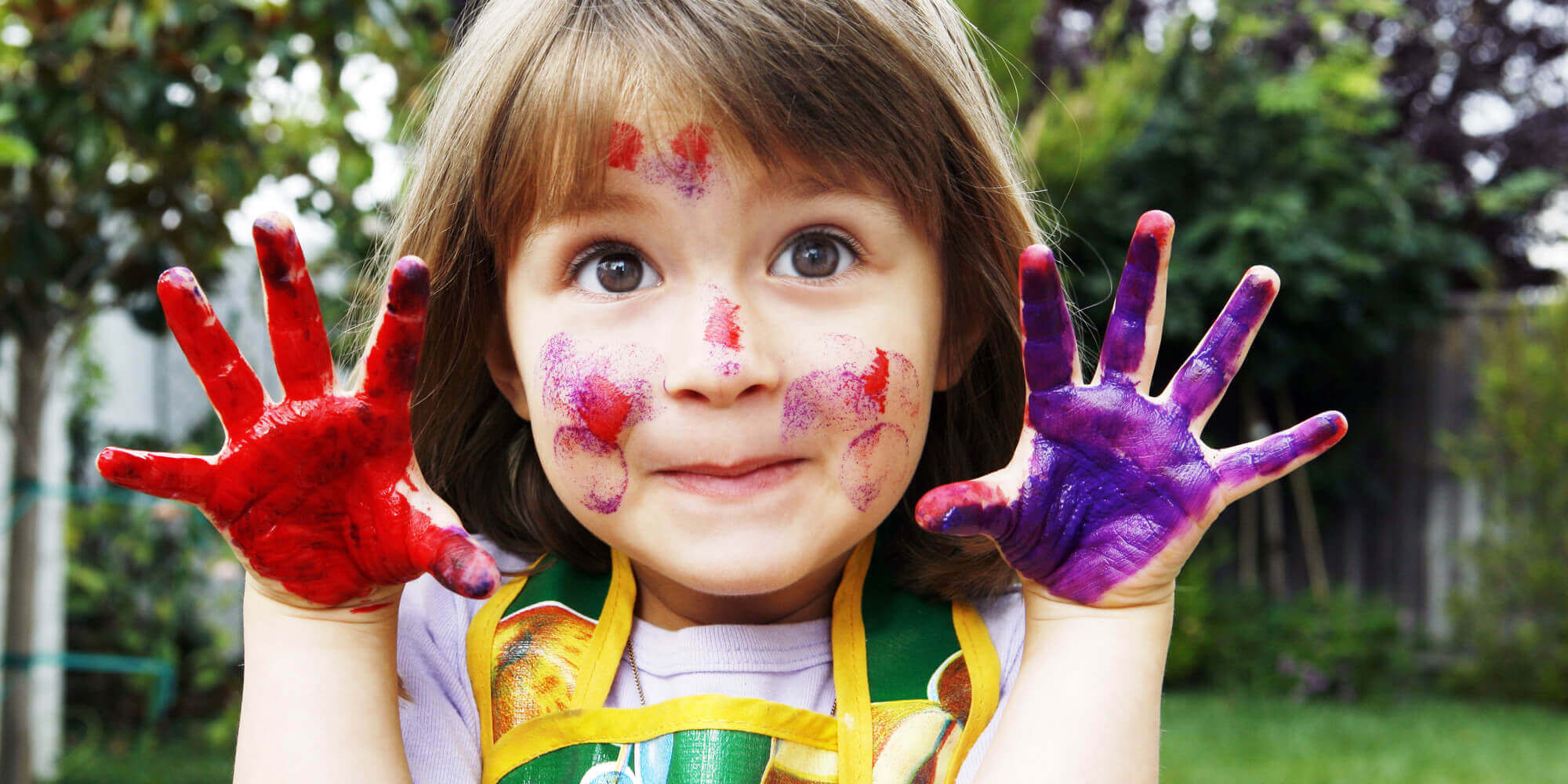 En liten jente med fingermaling på hendene og ansiktet.