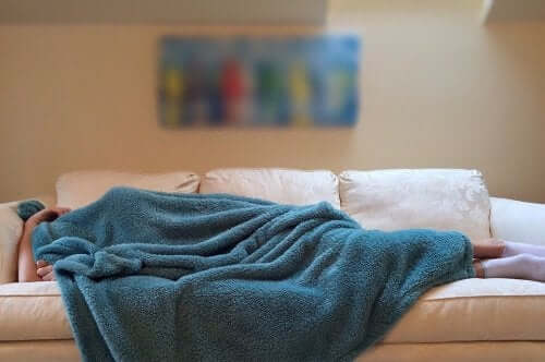 A person lying on a couch covered in a blanket.