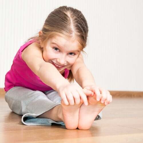 A little girl sitting on the floor touching her toes.