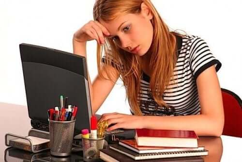 A teenage girl looking distracted while doing schoolwork on her computer.