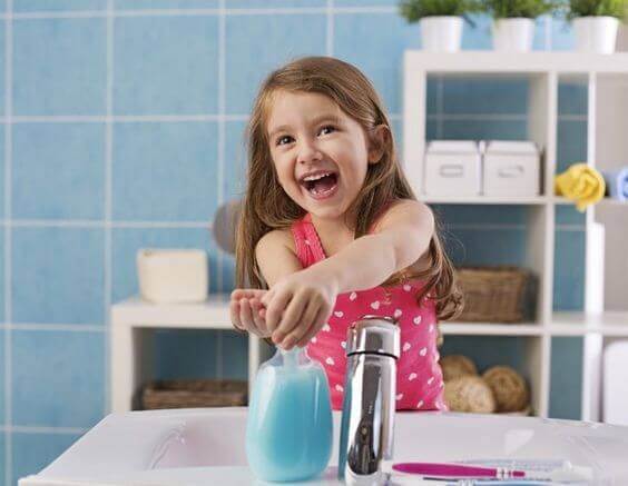 A little girl washing her hands and smiling.