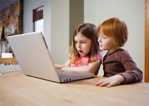 Two young children looking at the screen of a laptop.