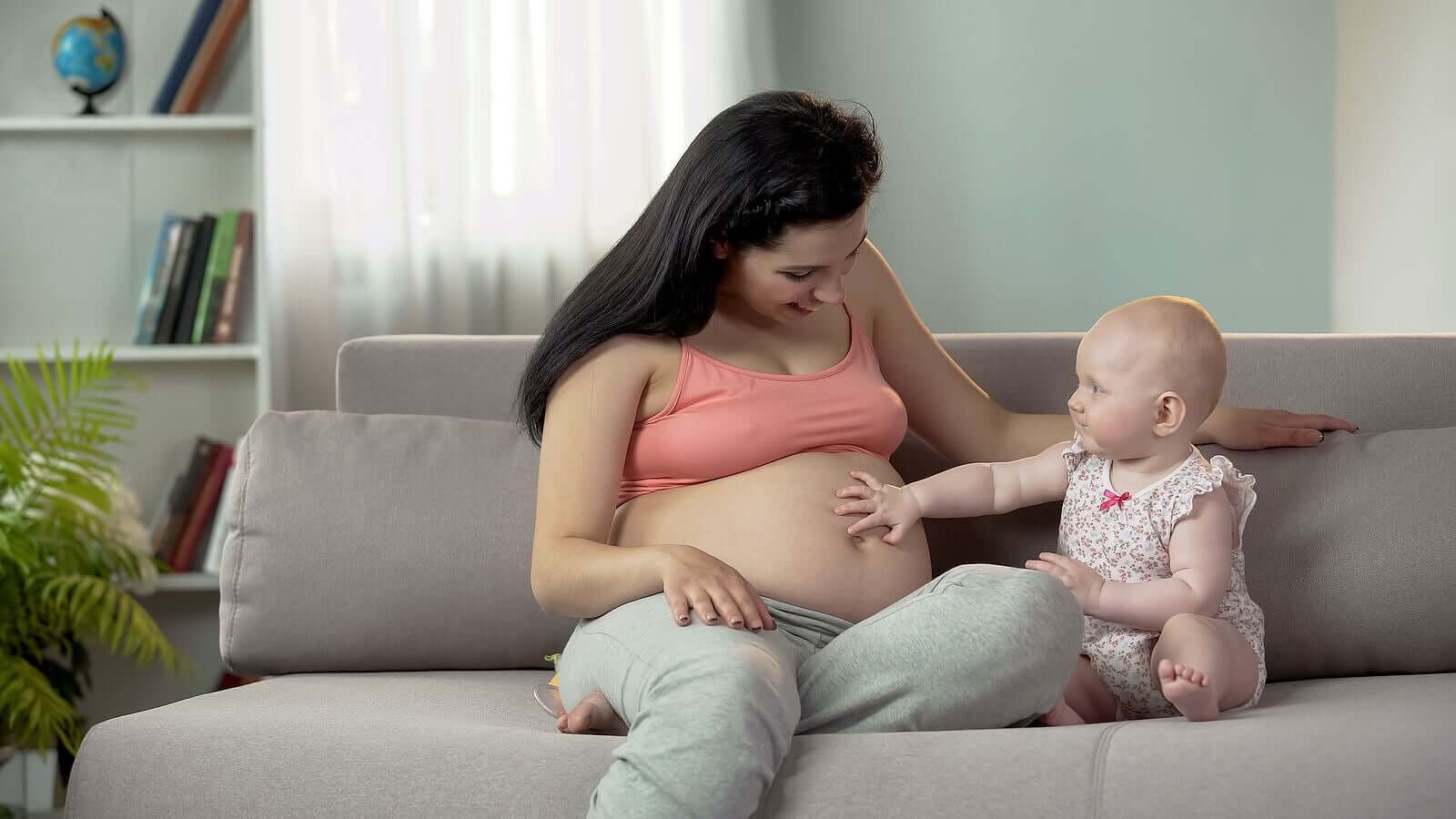 A baby girl touching her mother's pregnant belly.