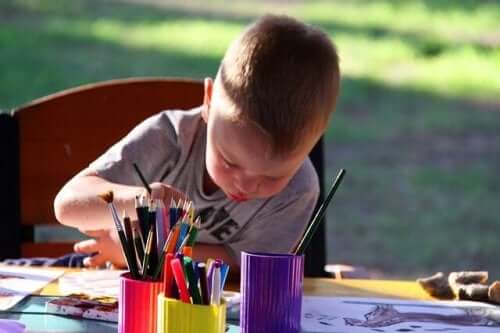 Ett barn målar vid ett bord utomhus.