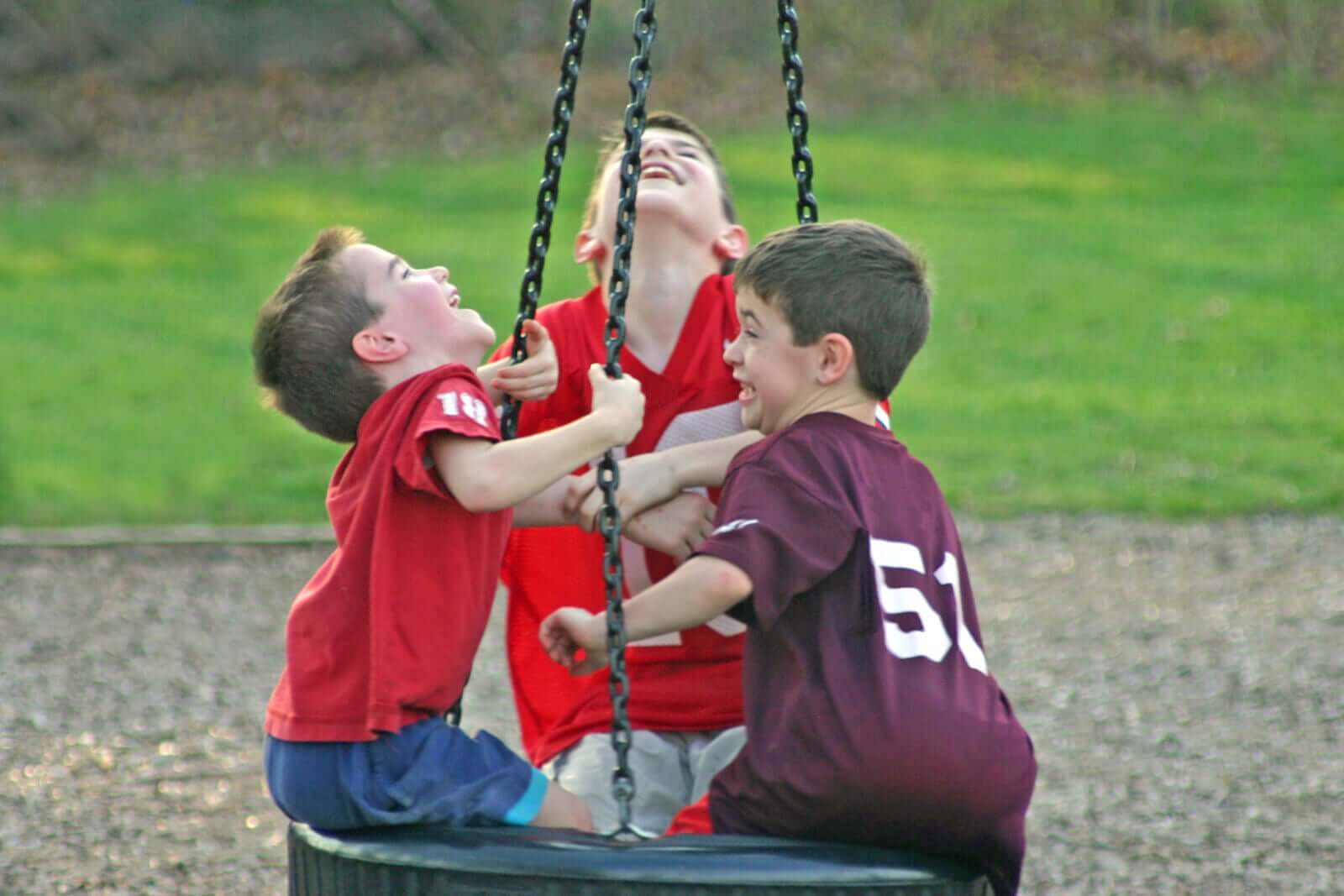 Three boys playing on a tire swing.