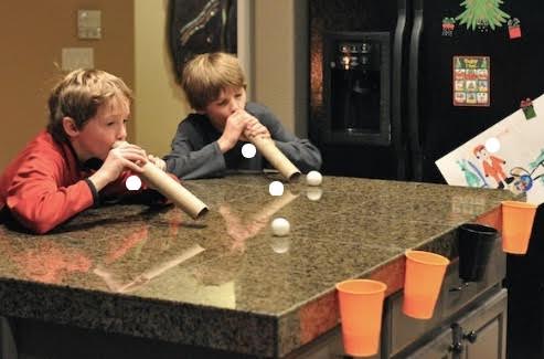 Children blowing on ping pong balls through cardboard tubes.