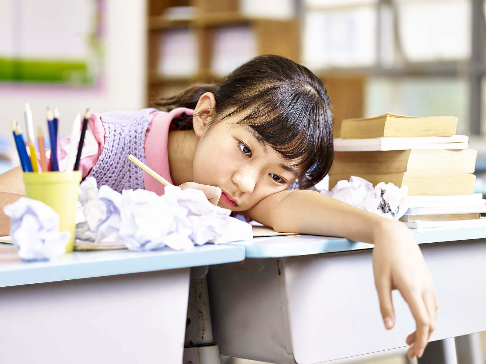A young girl with her head on her desk looking bored.