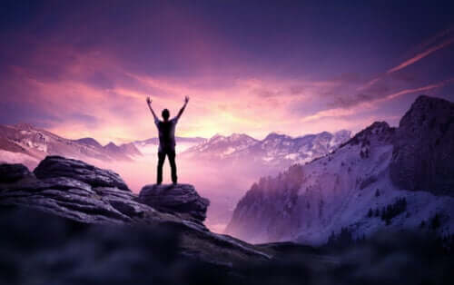 A man standing on a mountain with his hands in the air at sunrise.