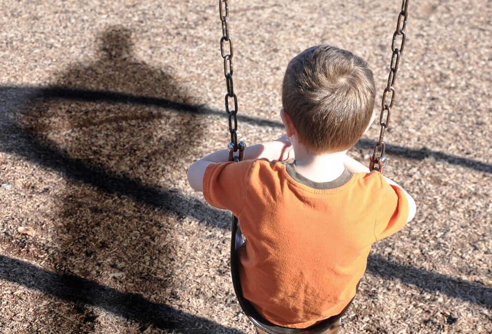 The shadow of a man over a child swinging in the park.