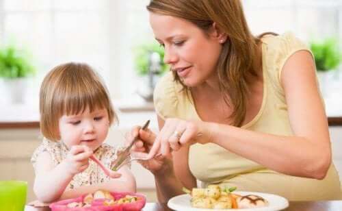 A mother cutting her toddler daughter's food for her.