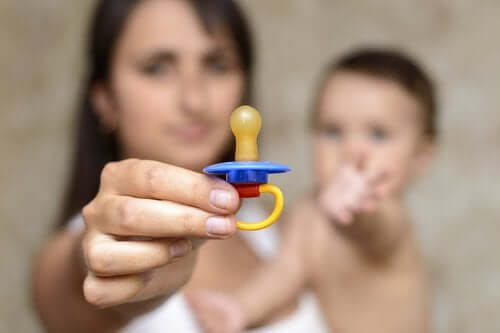 A mother holding a pacifier while her baby reaches for it.