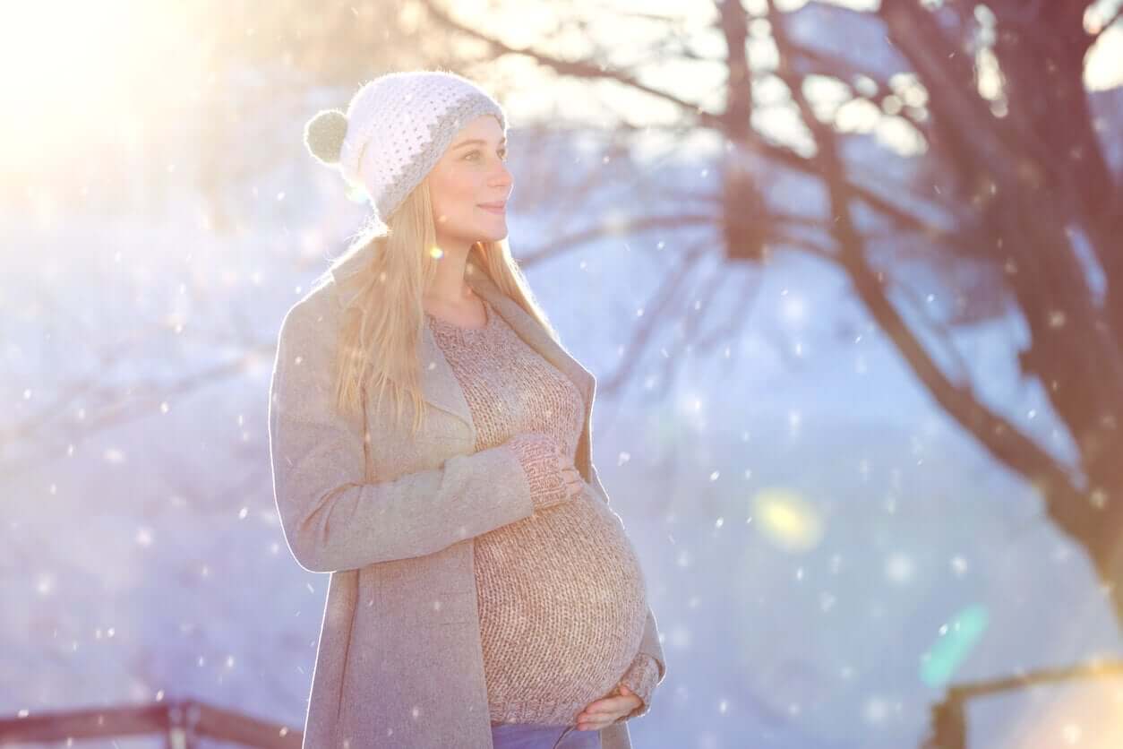 A blonde pregnant woman standing in the snow.