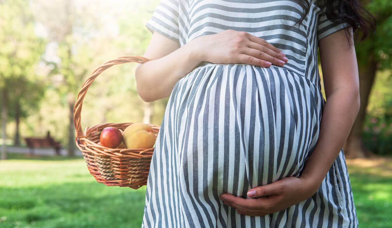 A mother cradling her pregnant belly while carrying a basket of fruit.