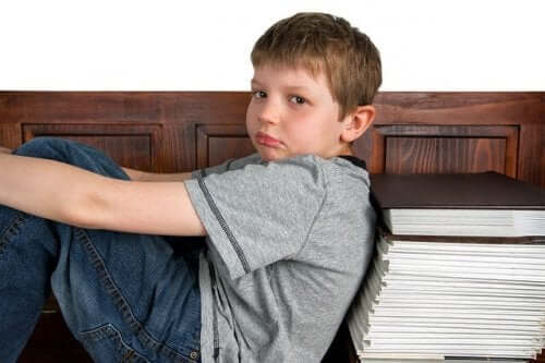 A child leaning sitting with his back against a pile of books, looking sad.