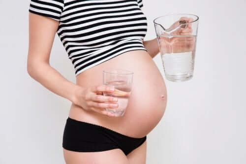 A pregnant woman pouring herself a glass of water.
