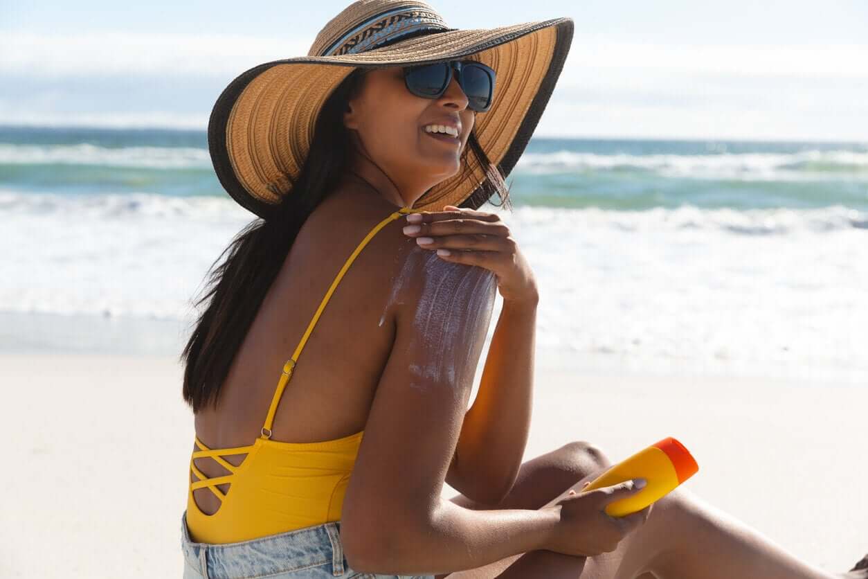 A woman putting sunscreen on her shoulder at the beach.