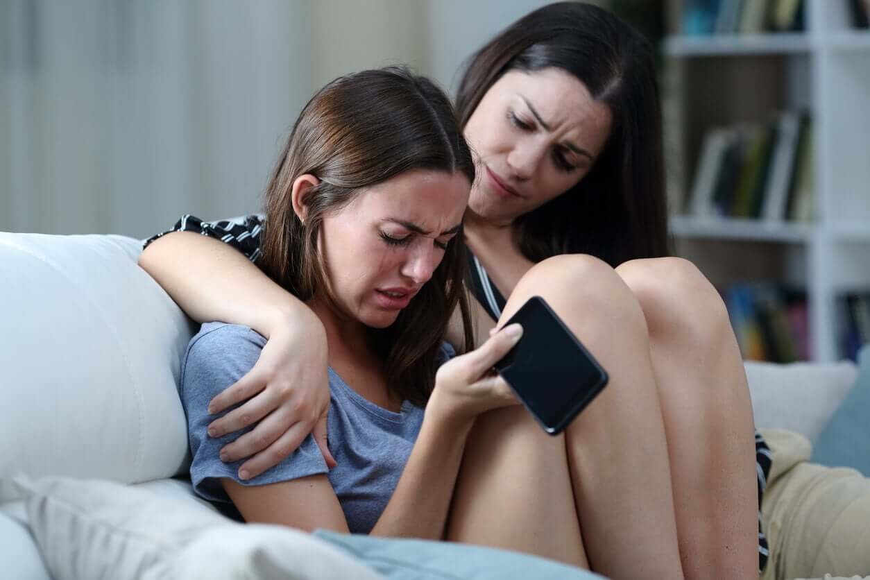 A woman comforting a teenage girl who's crying and holding a cell phone.