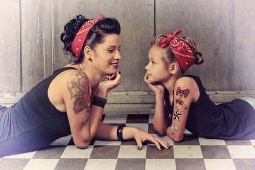 A mother and daughter dressed alike, lying on the floor, smiling at one another.