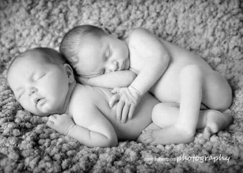 A black and white photo of newborn twins snuggling while they sleep.