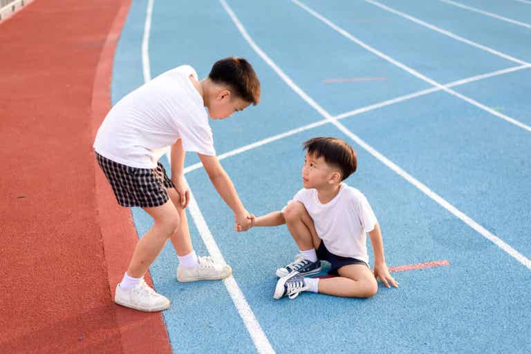 One boy helping another boy stand up after he's fallen on the track.