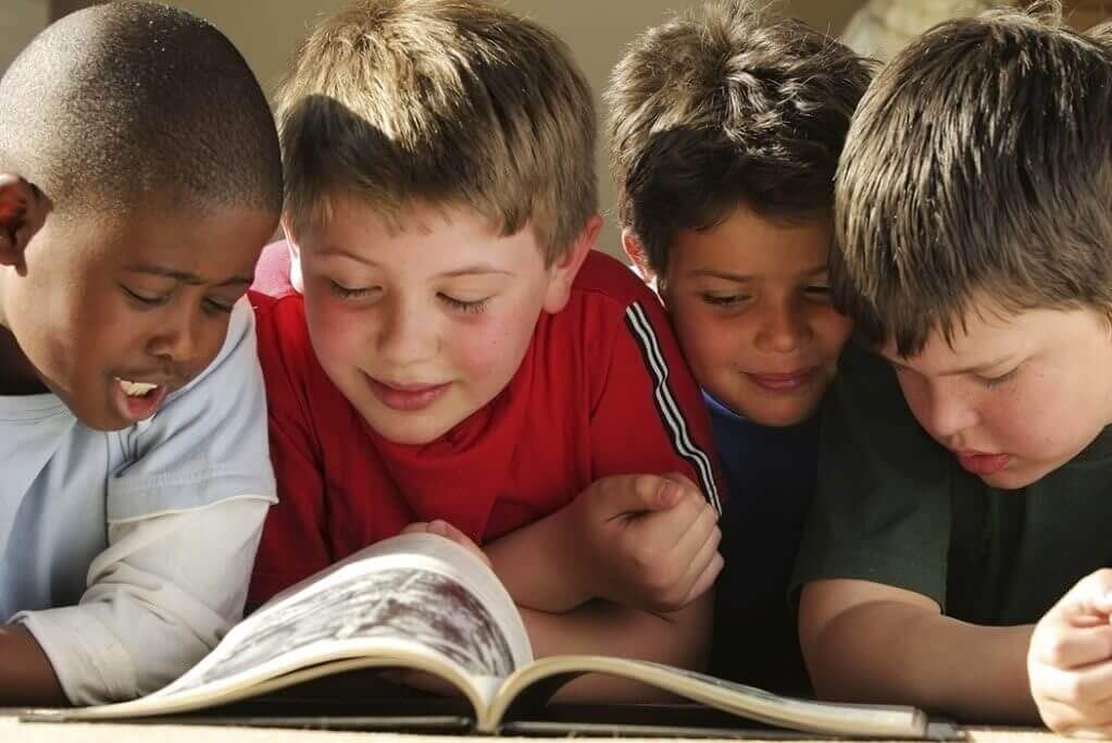 Four young boys reading a book together.