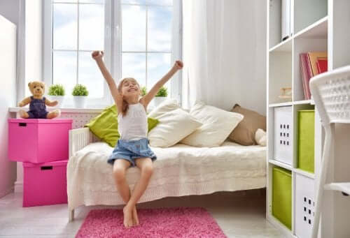 A little girl sitting on her bed, ligting her hands triumphantly.