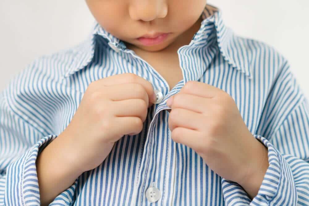 A small child buttoning his own shirt.