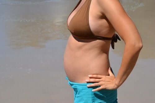 A women that's in her first trimester of pregnancy standing on the beach.
